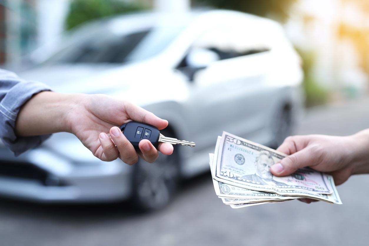 A hand reaching out with car keys in exchange for cash